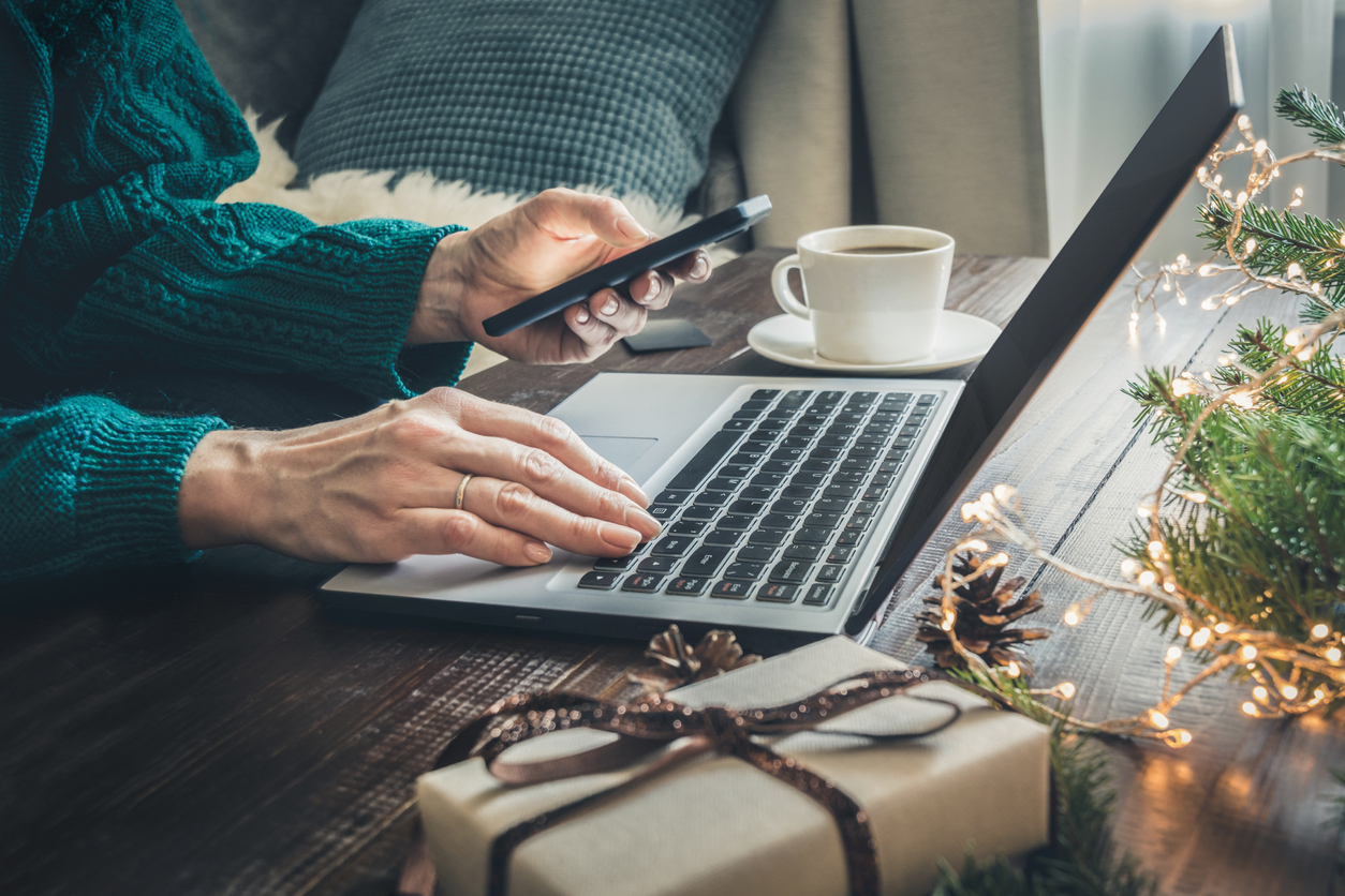 Christmas sales. Woman shopping with smartphone by laptop in home interior. Xmas. Planning holidays.